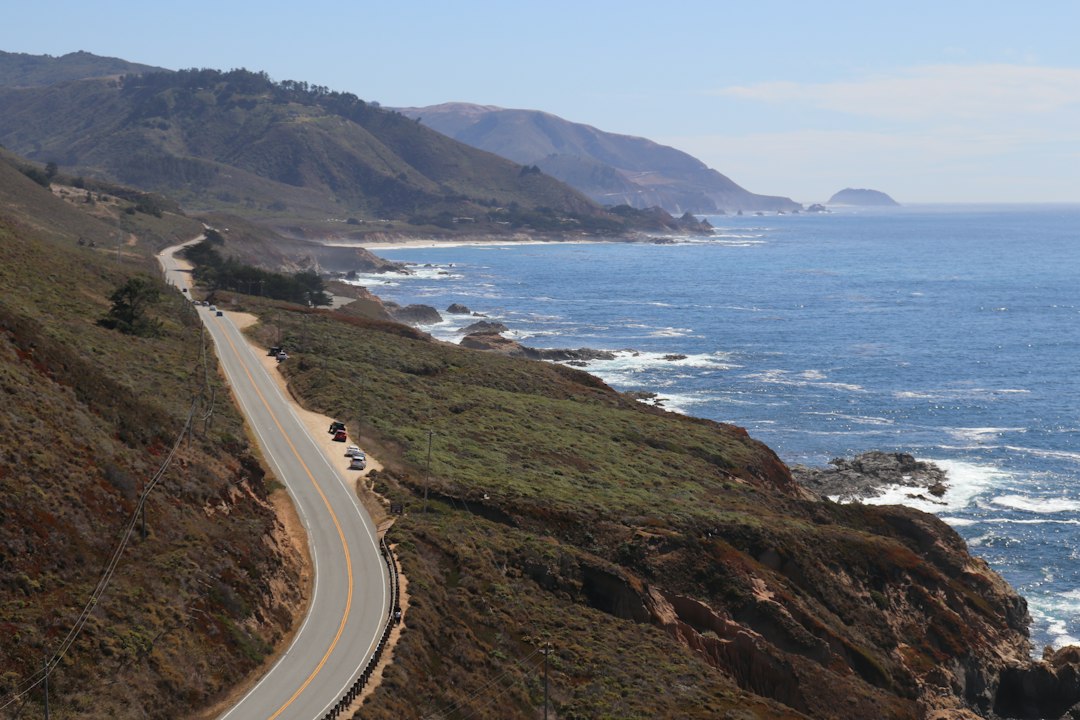 Pacific Coast Highway self-drive itinerary cover image featuring a cliffside highway, ocean views, and a convertible on Highway 1